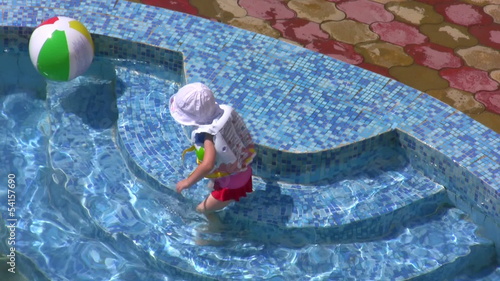 The little girl plays with a ball in water pool