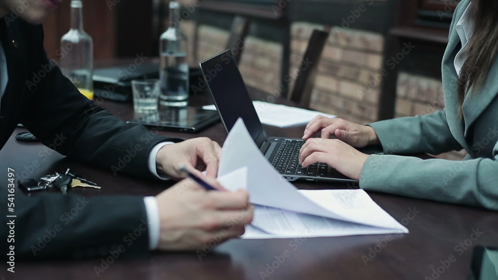 Businessman signing documents, businesswoman working on laptop