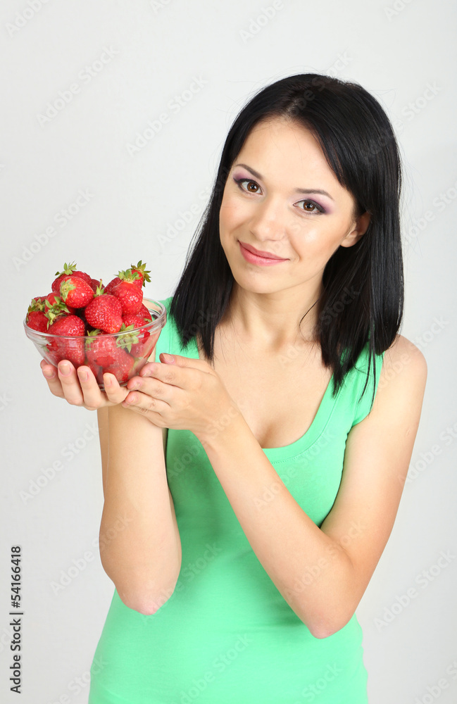 Beautiful young woman with strawberries on grey background Beautiful young woman with strawberries on grey background