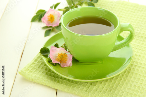 Cup of herbal tea with hip rose flowers on white wooden table