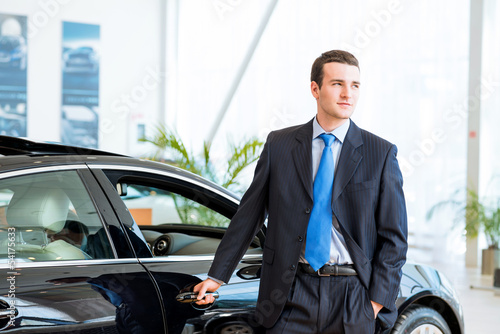 dealer stands near a new car in the showroom © adam121