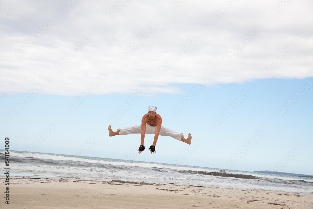 erwachsener sportlicher mann am strand springt karate