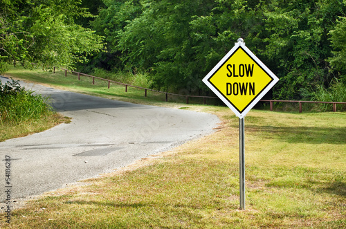 Foto Slow Down yellow traffic sign on the roadside against woods