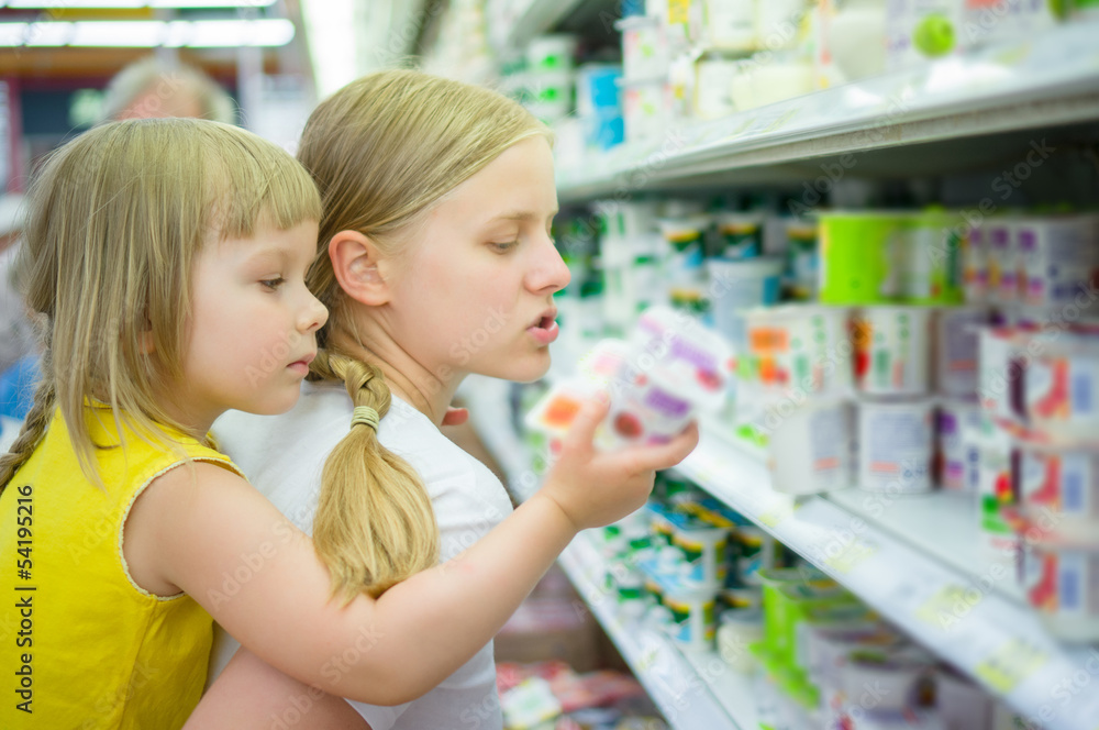 Mother with daughter on back select products in supermarket Mother with daughter on back select products in supermarket