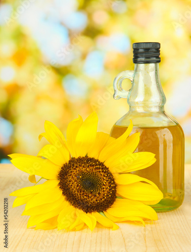 Oil in jar and sunflower on wooden table close-up