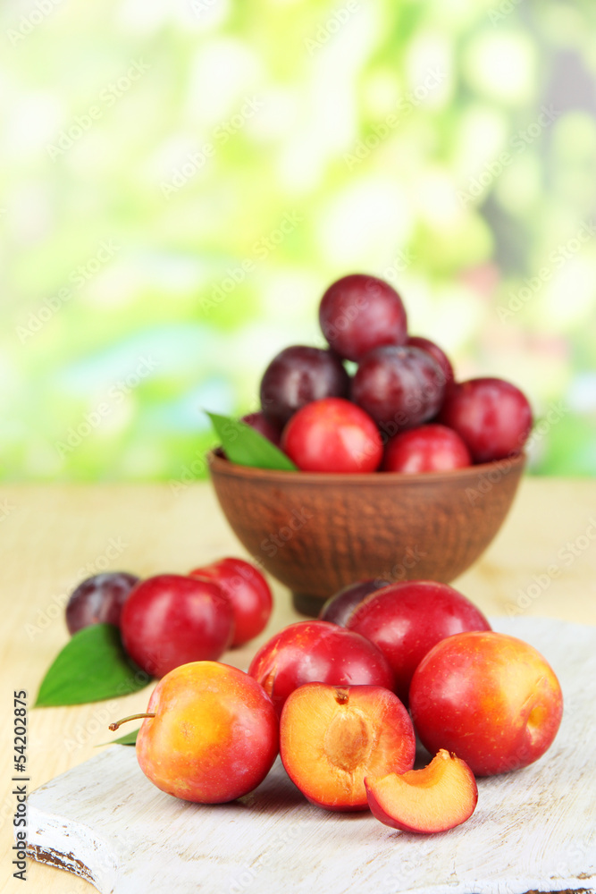 Ripe plums in bowl on wooden table on natural background Ripe plums in bowl on wooden table on natural background