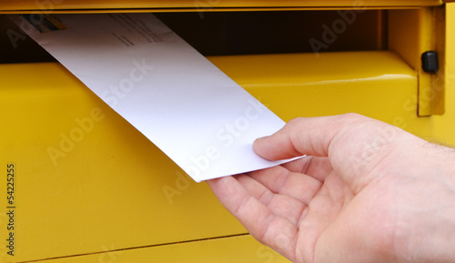Fotografía Menschliche Hand haltet einen Brief vor der gelben Briefkasten