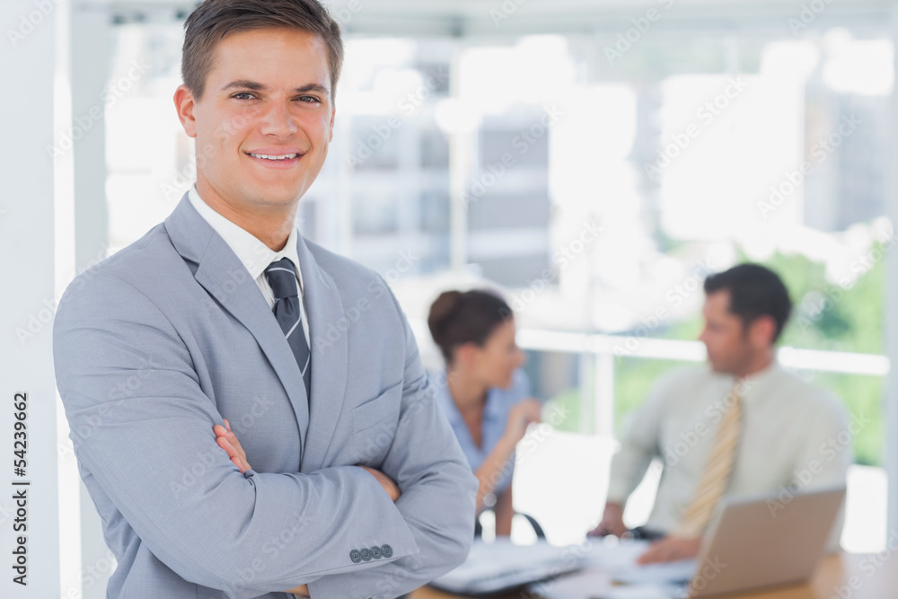 Smiling businessman and his colleagues in background Smiling businessman and his colleagues in background