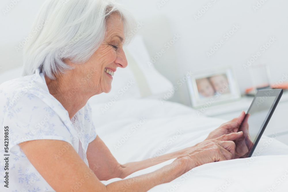 Woman using a tablet while she is lying on bed Woman using a tablet while she is lying on bed