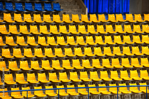 Plenty of yellow and blue plastic seats at stadium .