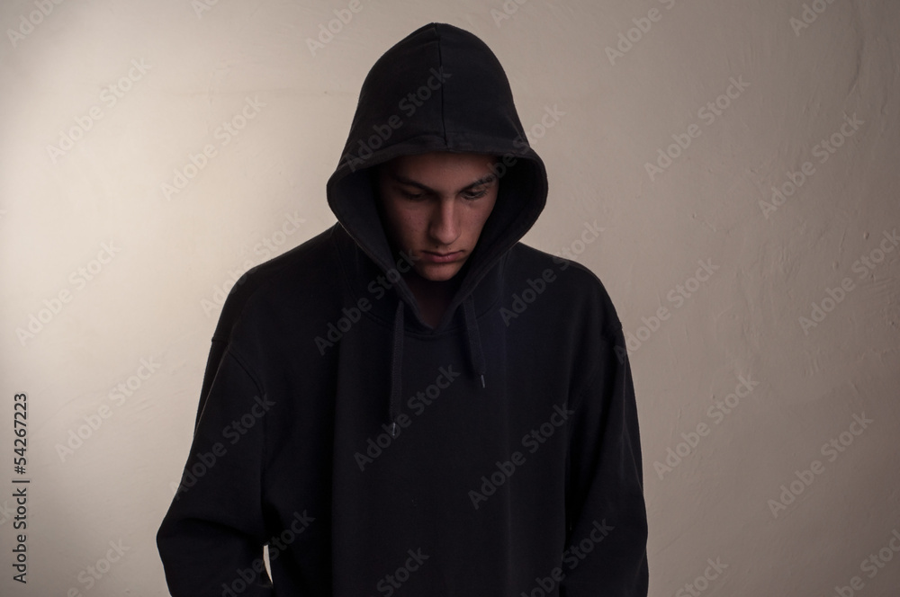 teenager with hoodie looking down against a dirty gray wall teenager with hoodie looking down against a dirty gray wall