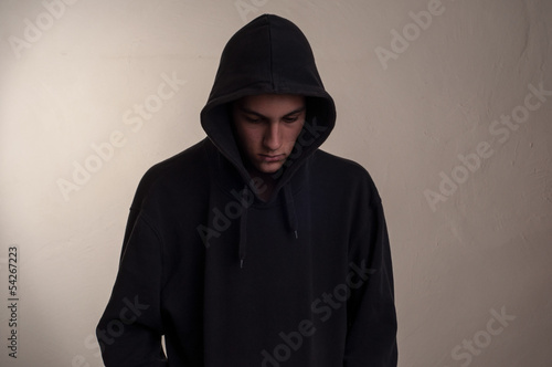 teenager with hoodie looking down against a dirty gray wall