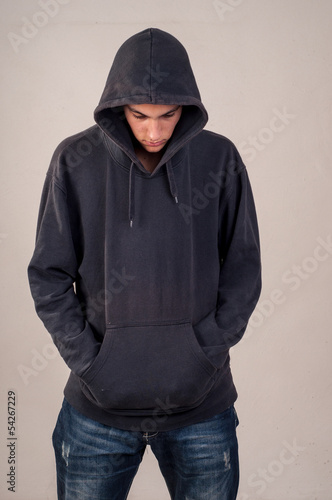 teenager with hoodie looking down against a dirty gray wall