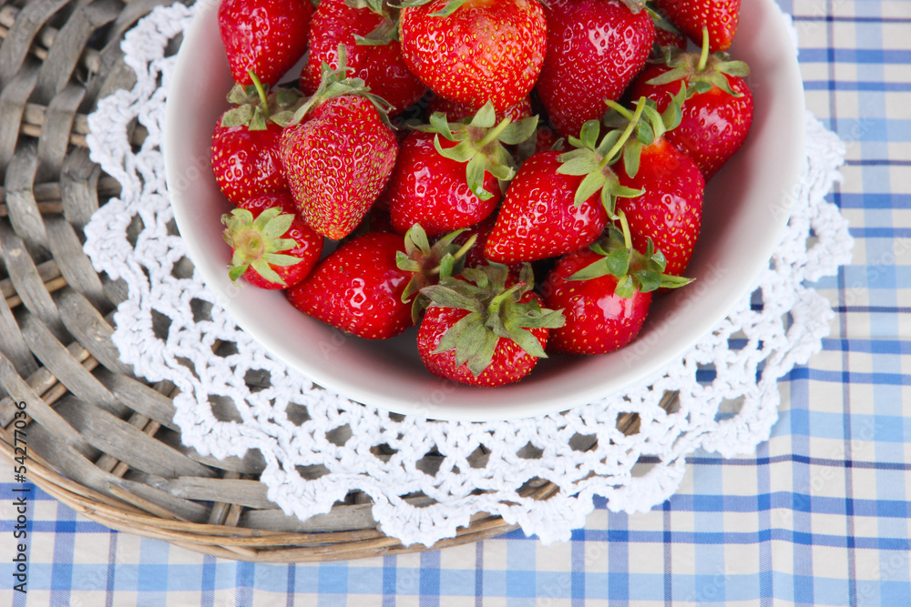 Strawberries in plate on wicker stand on napkin close-up