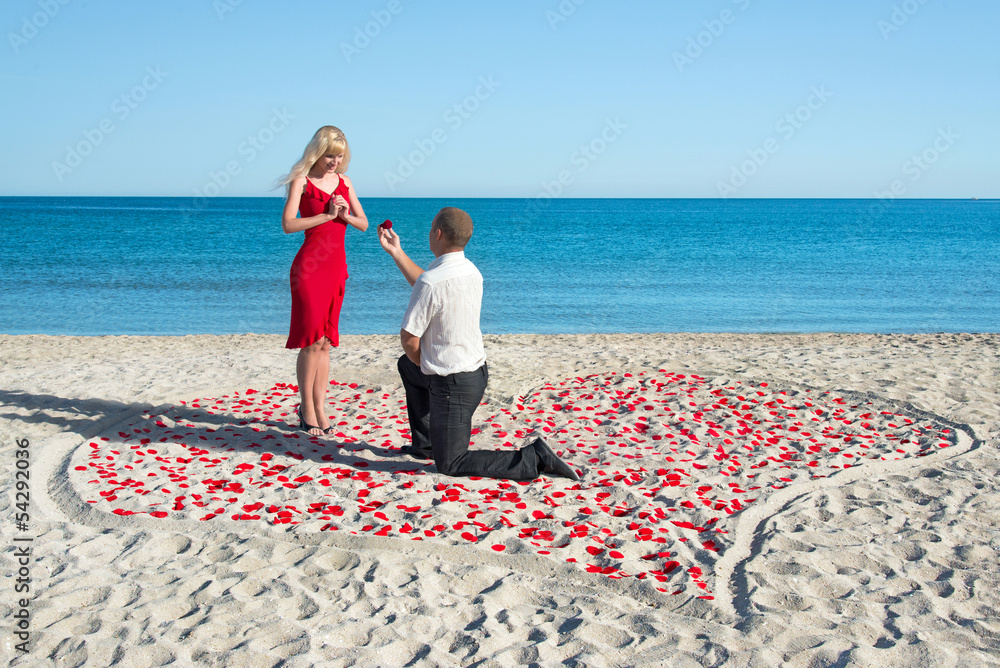 © EMrpize - man making proposal to his woman in the heart of roses petals on