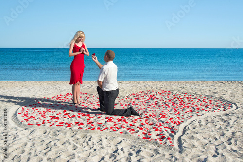 man making proposal to his woman in the heart of roses petals on