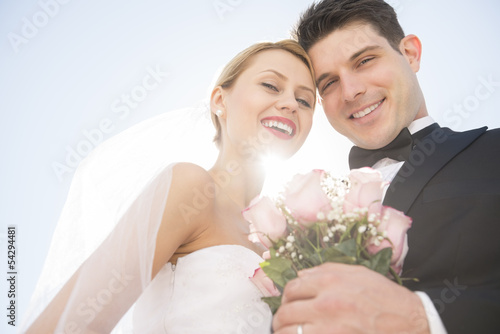 Newlywed Couple With Flower Bouquet Smiling Against Clear Sky