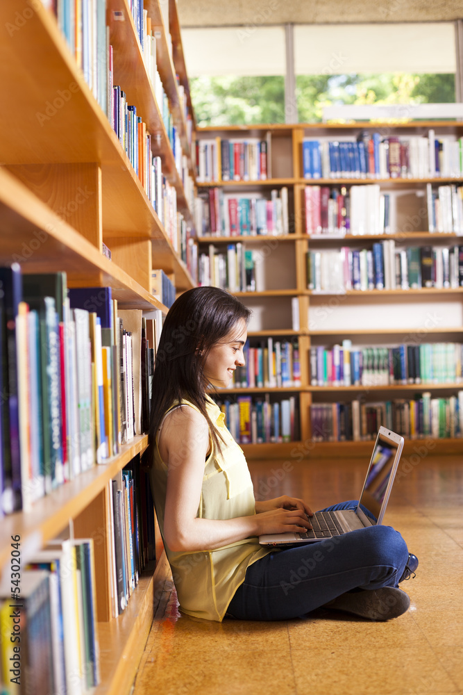 Young smiling student using her laptop in a library Young smiling student using her laptop in a library