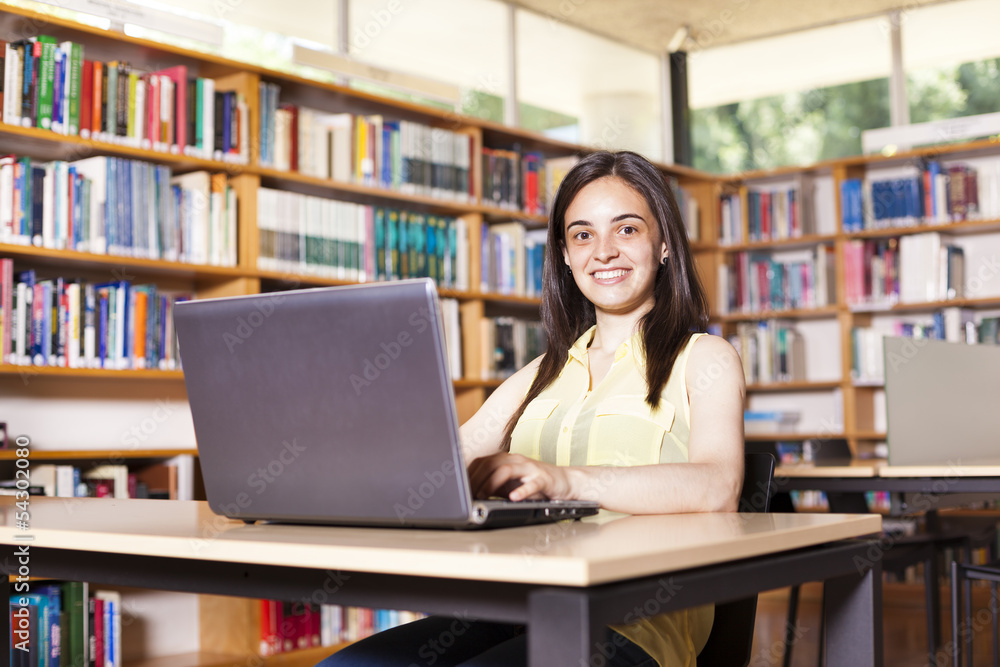 Smiling female student working with laptop in a high school libr Smiling female student working with laptop in a high school libr