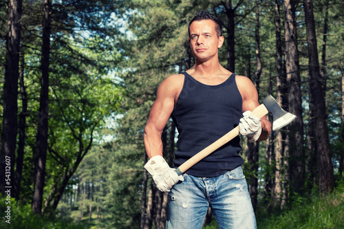 Muscled man with black shirt and axe in forest.
