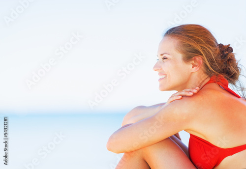 Happy young woman sitting on beach and looking on copy space