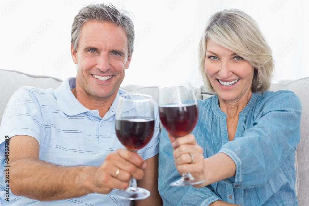 Couple toasting to the camera with red wine on the sofa Couple toasting to the camera with red wine on the sofa