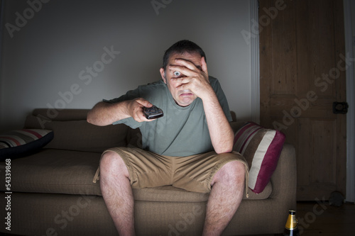 man covering his eyes watching tv
