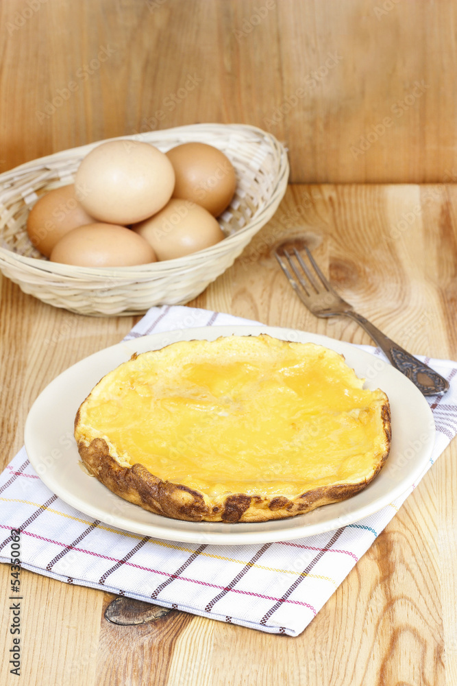 Omelette on wooden table. Basket with eggs in the background Omelette on wooden table. Basket with eggs in the background