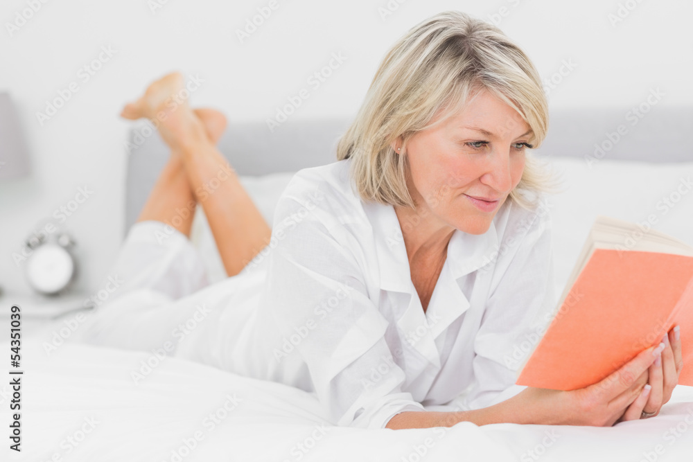 Cheerful woman reading a book lying on bed Cheerful woman reading a book lying on bed