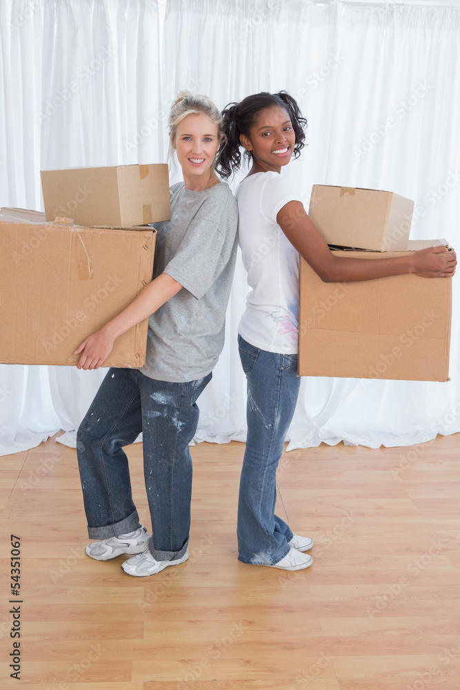 Smiling friends standing back to back holding moving boxes Smiling friends standing back to back holding moving boxes