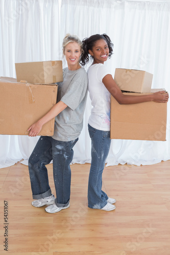 Smiling friends standing back to back holding moving boxes © WavebreakmediaMicro