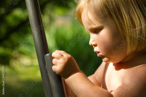 Young child exploring and touching a metal bar in the garden