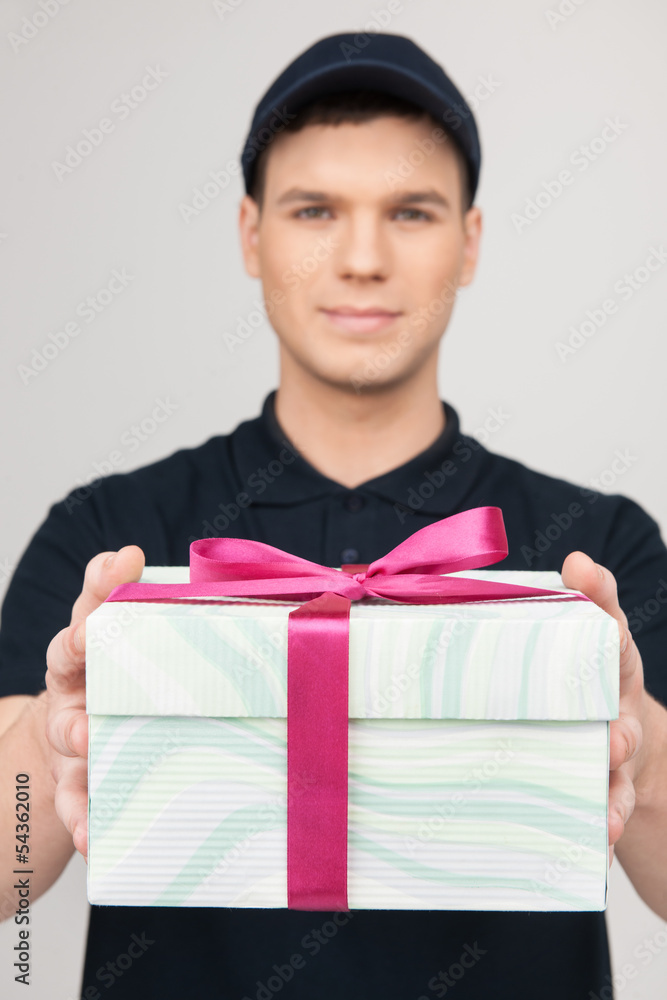 Delivering a present. Cheerful young deliveryman holding a gift Delivering a present. Cheerful young deliveryman holding a gift