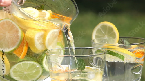 Close-up of jug with fresh lemonade pouring to glass.