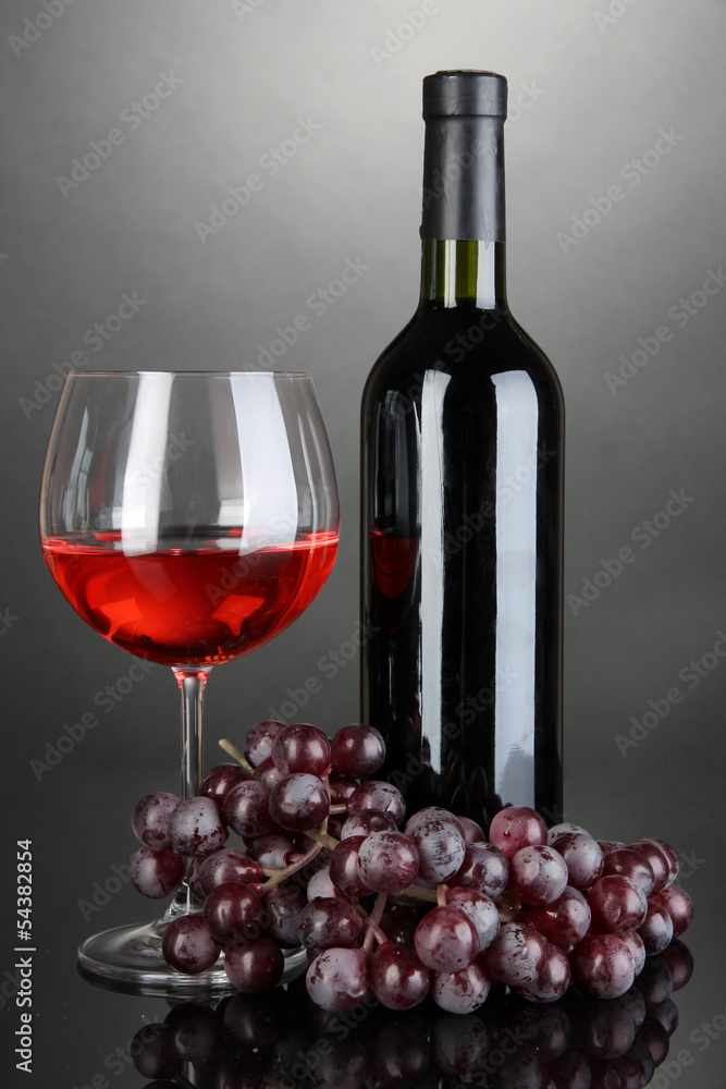 Obraz premium Red wine glass and bottle of wine on grey background