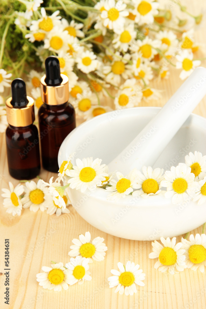 Essential oil and chamomile flowers in mortar on wooden table Essential oil and chamomile flowers in mortar on wooden table