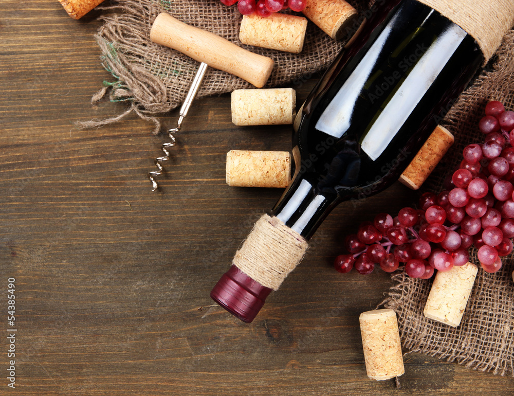 Bottle of wine, grapes and corks on wooden background