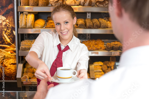 Saleswoman in baker's shop giving cup of coffee to customer