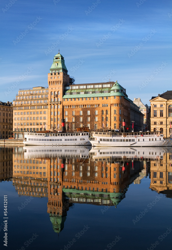 Old steam boats and buildings reflecting in water in Stockholm.