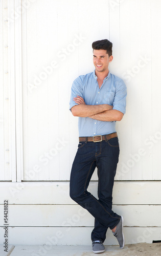 Handsome young man standing outdoors against white wall