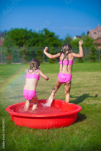 Two little sisters frolicing and splashing in their yard in photo