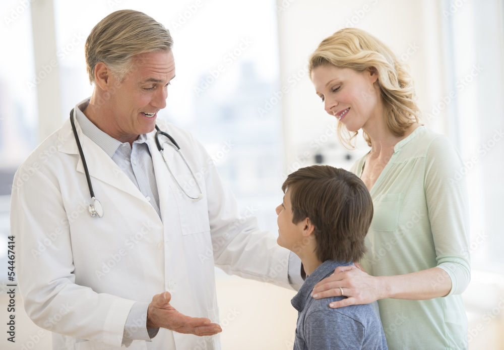 Doctor Explaining Boy While Mother Looking At Him In Clinic Doctor Explaining Boy While Mother Looking At Him In Clinic