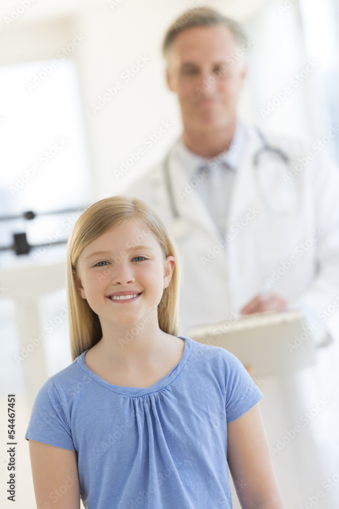 Fototapeta premium Girl Smiling With Doctor Standing In Background At Clinic