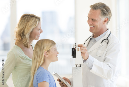Doctor Examining Girl s Weight While Looking At Woman In Clinic
