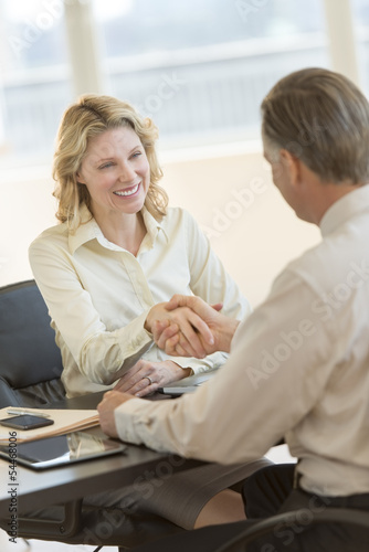 Businesswoman Shaking Hands With Colleague At Desk