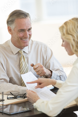 Businessman Looking At Colleague Reading Document In Office