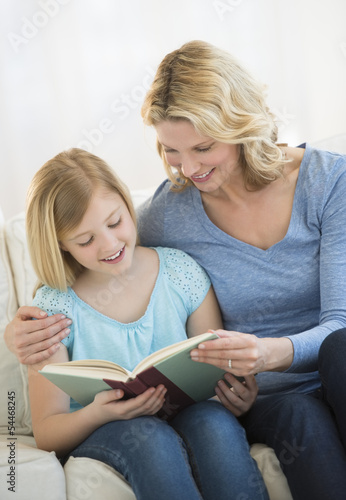 Mother And Daughter Reading Book Together At Home