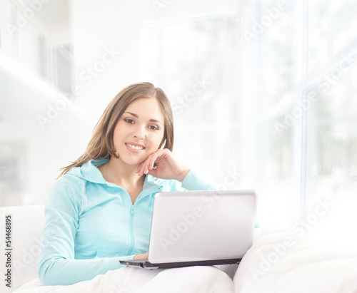 A young brunette woman with a laptop relaxing on a white sofa