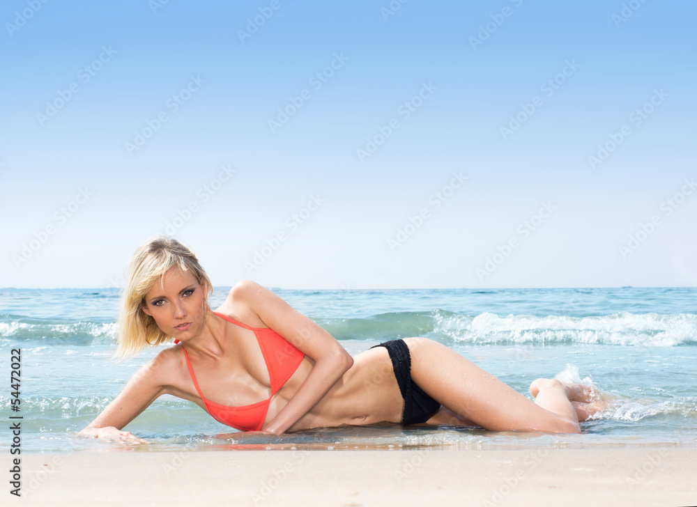 A young blond woman laying on a beach background