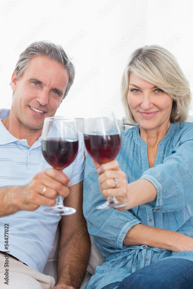 Couple toasting to the camera with red wine on the couch Couple toasting to the camera with red wine on the couch